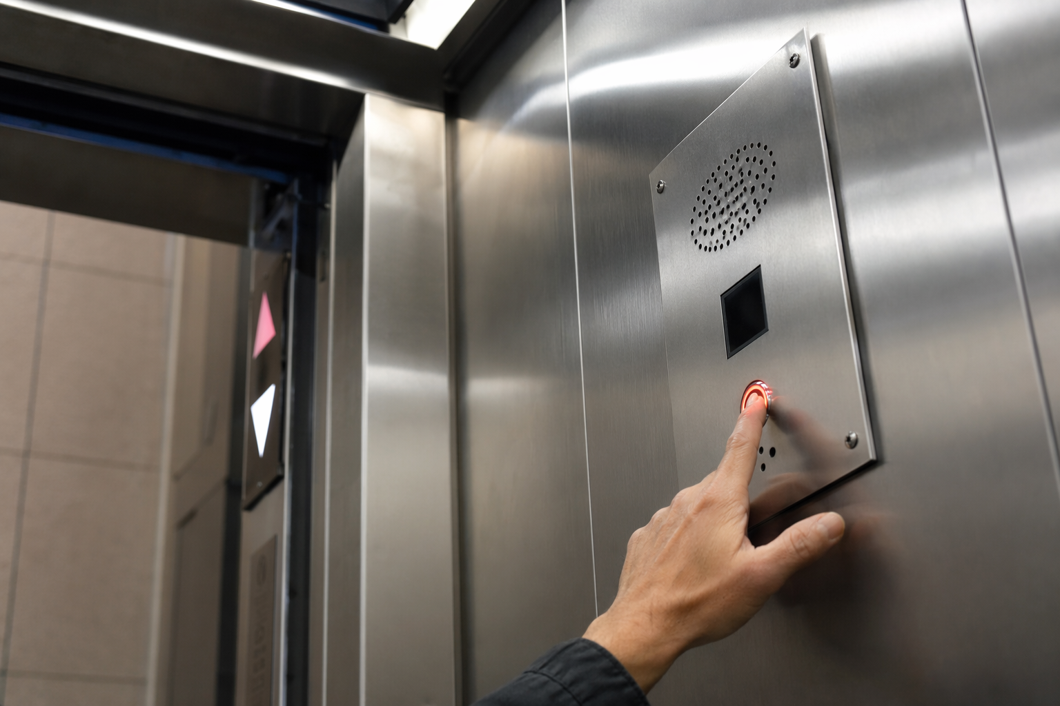 Elevator passenger pressing the emergency call button inside a stalled cab between floors, illustrating an entrapment scenario requiring immediate elevator breakdown response.