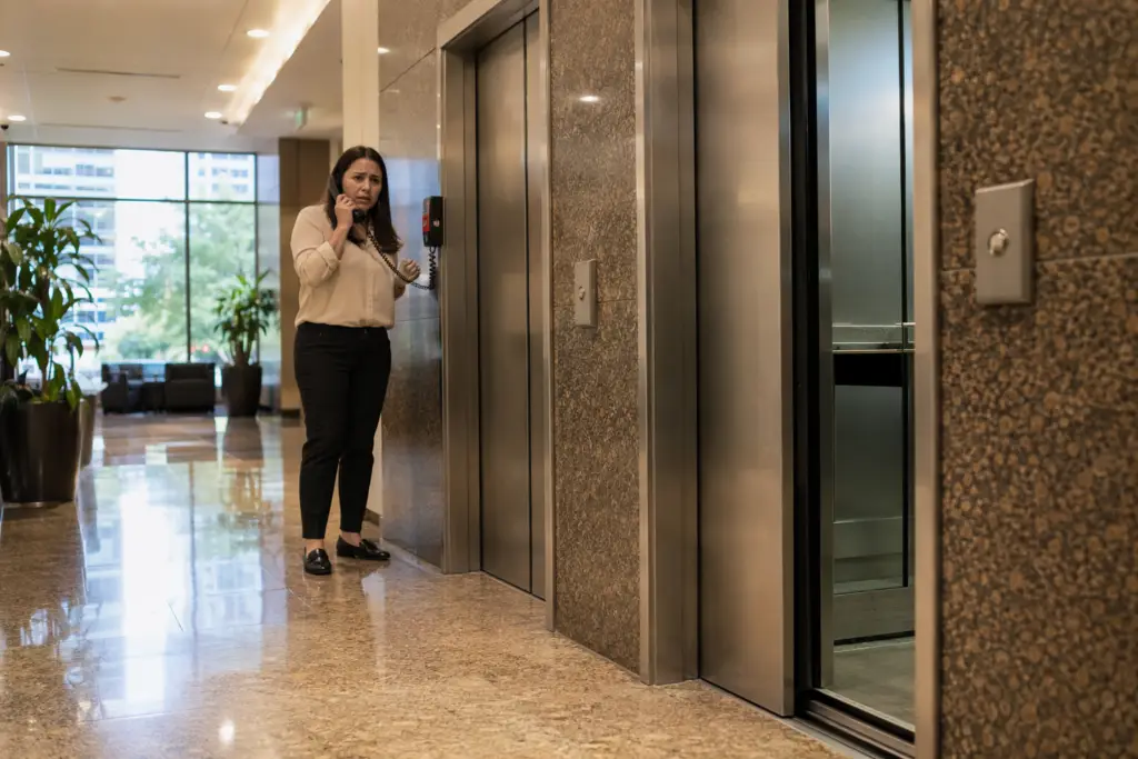 Building manager contacts elevator service contractor for immediate response to elevator breakdown in Houston commercial office lobby, following ASME A17.1 emergency protocol.