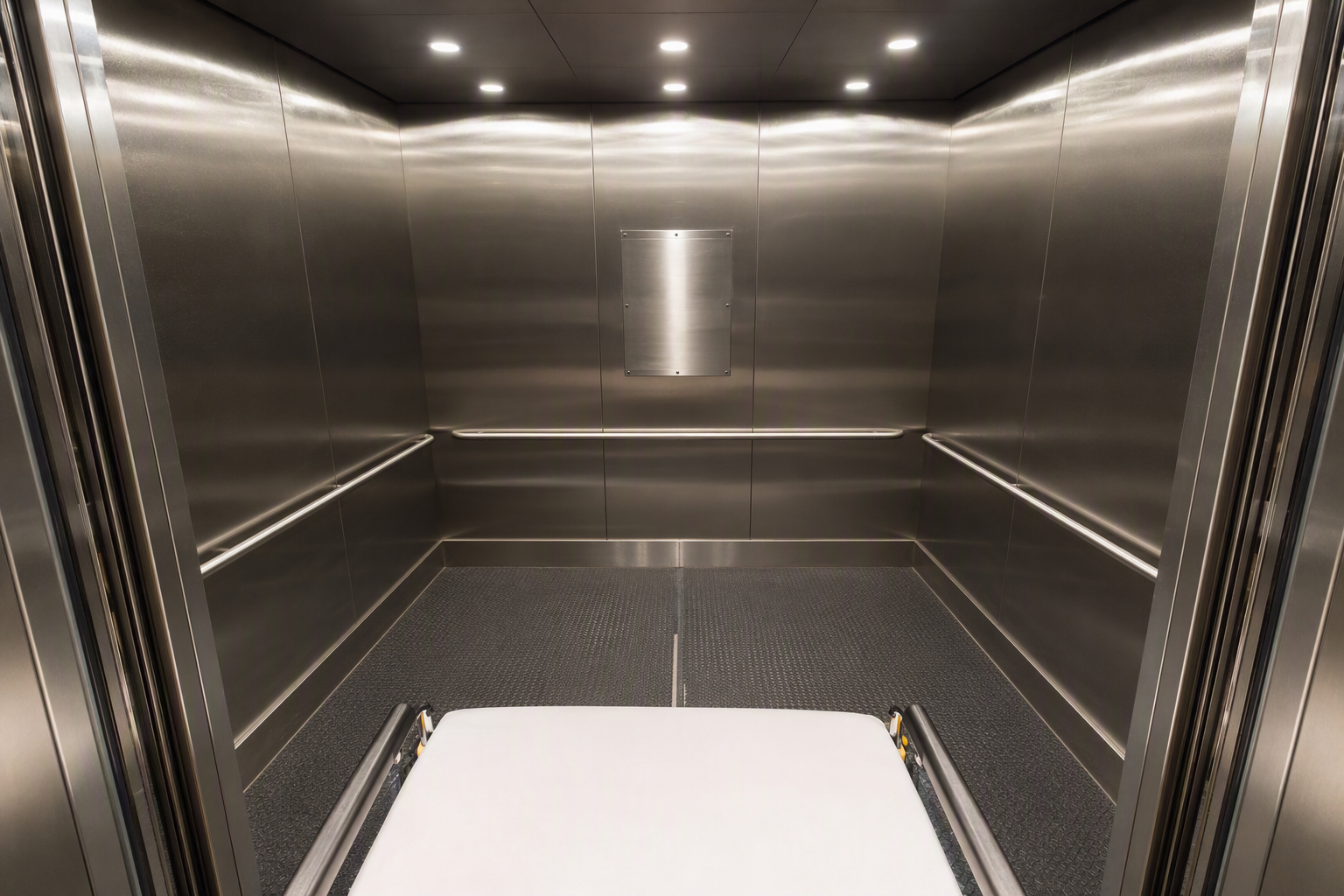 Wide hospital elevator cab interior showing ASME A17.1 load capacity placard, full-width handrails, and non-slip flooring meeting California commercial building elevator code requirements for healthca
