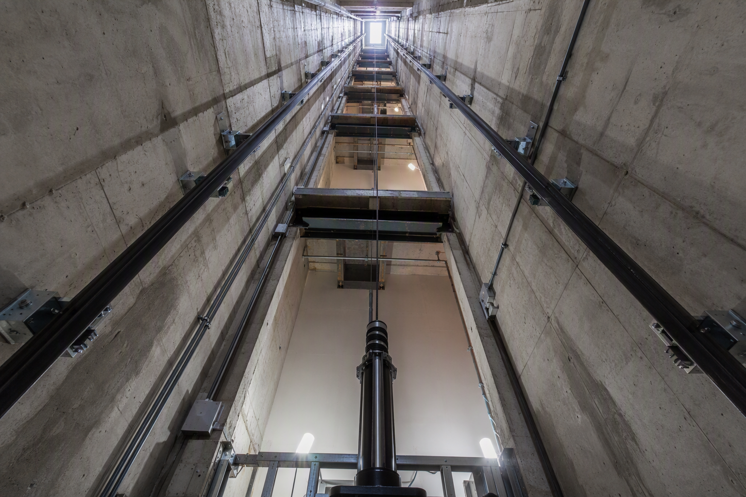 New commercial elevator hoistway under construction in a Houston office building, showing steel guide rails, concrete walls, and hydraulic pit — key cost driver for elevator installation.
