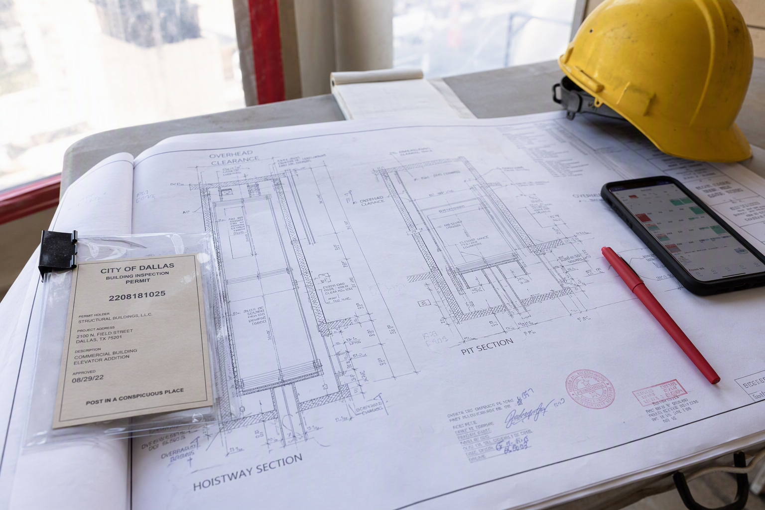 Elevator Permit Drawings and Project Schedule Coordination Stamped elevator installation engineering drawings and building permit documents laid out on a job-site table during a commercial elevator retrofit project permitting phase in Dallas TX.