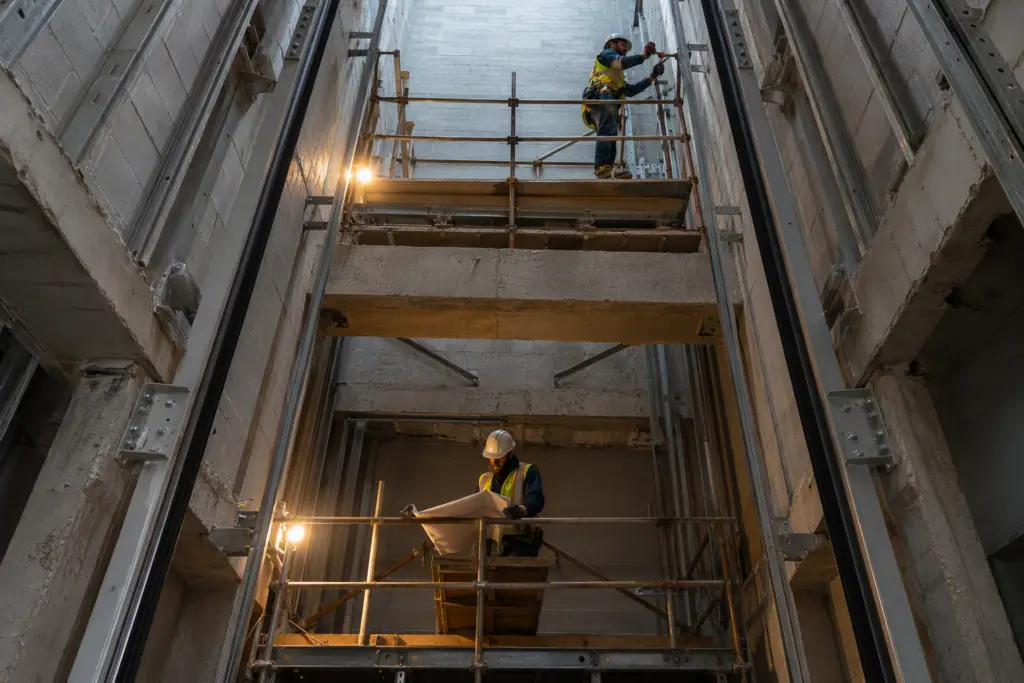 Elevator installation hoistway under construction in an existing Houston commercial office building, showing guide rail work and multi-floor scaffolding during a new elevator retrofit project.
